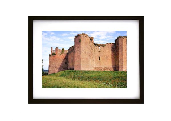 Side view of the red sandstone walls and towers of Bothwell Castle, a medieval ruin in Scotland, under a blue sky with light clouds.