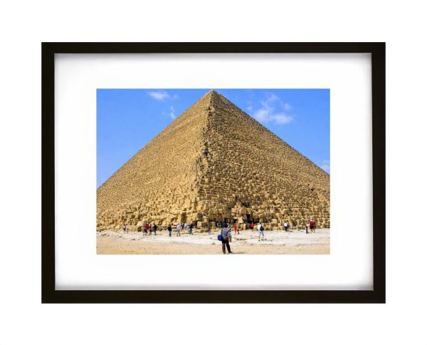 A powerful landscape photograph showing the Great Pyramid of Cheops at Giza, Egypt. Camels and visitors in the foreground emphasise the scale and enduring presence of this ancient wonder beneath a bright desert sky.